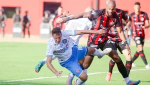 BA-VI: árbitro explica acréscimos polêmicos em primeiro jogo da final do Baianão Foto: Tiago Caldas | EC Bahia Neste domingo (31), Bahia e Vitória protagonizaram um clássico polêmico pela primeira final do Campeonato Baiano. Tudo isso porque o gol do triunfo saiu aos 53 minutos do 2º tempo, e os acréscimos viraram motivo de revolta nas redes sociais, com a suposta demora do árbitrio para encerrar a partida. Na súmula, divulgada pela Federação Baiana de Futebol, o juiz Bruno Pereira Vasconcelos, explicou a situação. A polêmica se deu após o quarto árbitro levantar a placa de acréscimos mostrando 5 minutos. Em seguida, ele comunicou mais um minuto, totalizando seis. Ou seja, o duelo terminaria aos 51 minutos do segundo tempo. Após o gol, marcado aos 53, a partida só foi encerrada aos 55. Na súmula, o árbitro explicou que a placa de acréscimos foi levantada somente aos 47 minutos do segundo tempo, já que a equipe de arbitragem estava gerenciando a comemoração do gol de empate do Vitória, que aconteceu aos 45. Com isso, foi informada às equipes que os minutos de acréscimos sinalizados pela placa valeriam a partir dos 47. Em seguida, foi acrescido mais um minuto. "INFORMO QUE A PLACA DE ACRÉSCIMO FOI LEVANTADA AOS 47 MINUTOS DO 2 TEMPO, DECORRENTE À EQUIPE DE ARBITRAGEM ESTAR GERENCIANDO A COMEMORAÇÃO DE GOL DO E. C. VITORIA, QUE OCORREU AOS 45 MINUTOS, MOMENTO EM QUE DEVERIA TER SIDO SINALIZADO, COM ISSO FOI INFORMADO ÀS EQUIPES QUE OS 05 MINUTOS DE ACRÉSCIMOS SINALIZADOS PELA PLACA SE DEU A PARTIR DOS 47 MINUTOS, E A PARTIDA COM O TÉRMINO AOS 52 MINUTOS DO 2 TEMPO, TENDO AINDA MAIS 01 MINUTO ACRÉSCIDO. SOMANDO UM TOTAL DE 08 MINUTOS DE ACRÉSCIMO, FINALIZANDO A PARTIDA AOS 53 MINUTOS DO 2 TEMPO", diz trecho do documento. As equipes voltam a se enfrentar no próximo domingo, 7, na Arena Fonte Nova, pela partida decisiva da final. O Vitória pode até empatar que será campeão. O Bahia precisa vencer por dois gols de difença. Se o triunfo do Tricolor for por apenas um gol, a decisão do título fica para os pênaltis.